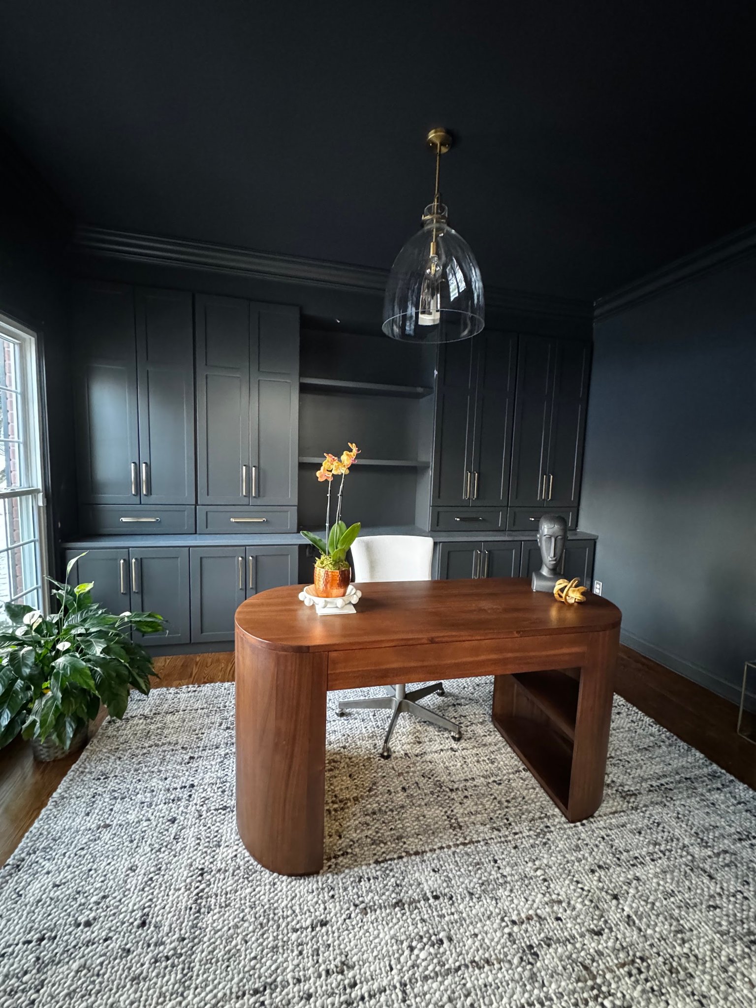 Dark built-in cabinetry, a warm wood desk, and a glass pendant give this Northern Kentucky home office a bold, polished look.